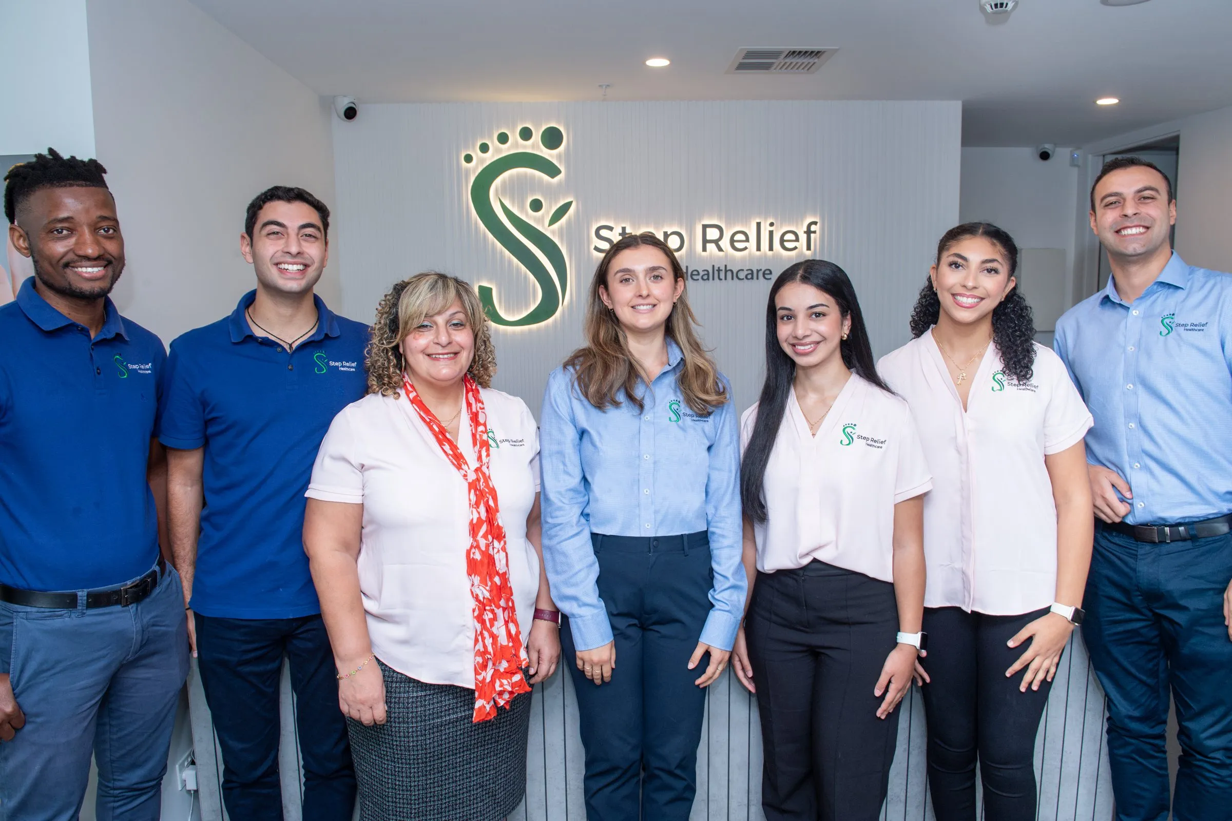 The Step Relief Healthcare team in matching uniforms standing in front of the clinic’s reception sign