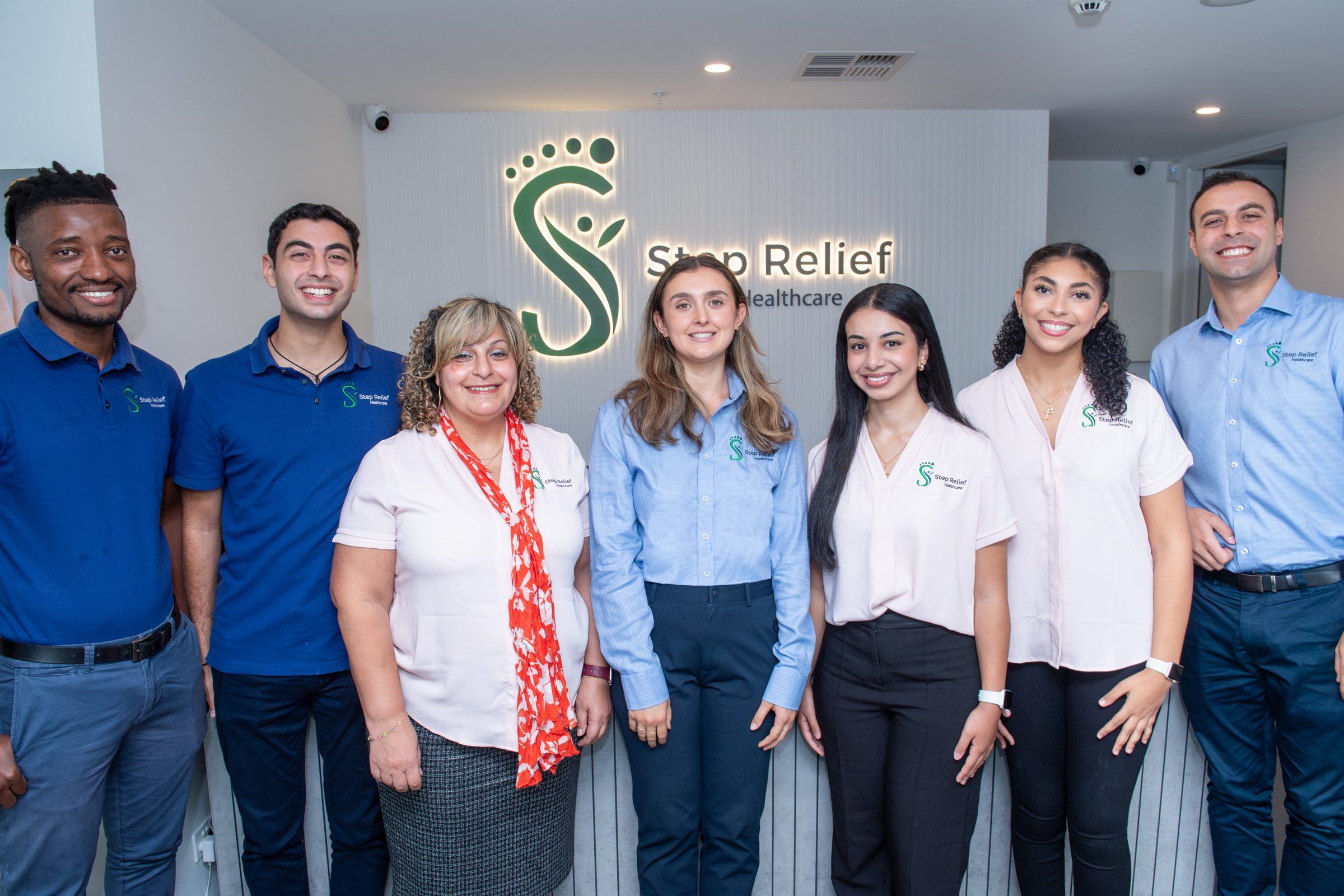 The Step Relief Healthcare team in matching uniforms standing in front of the clinic’s reception sign