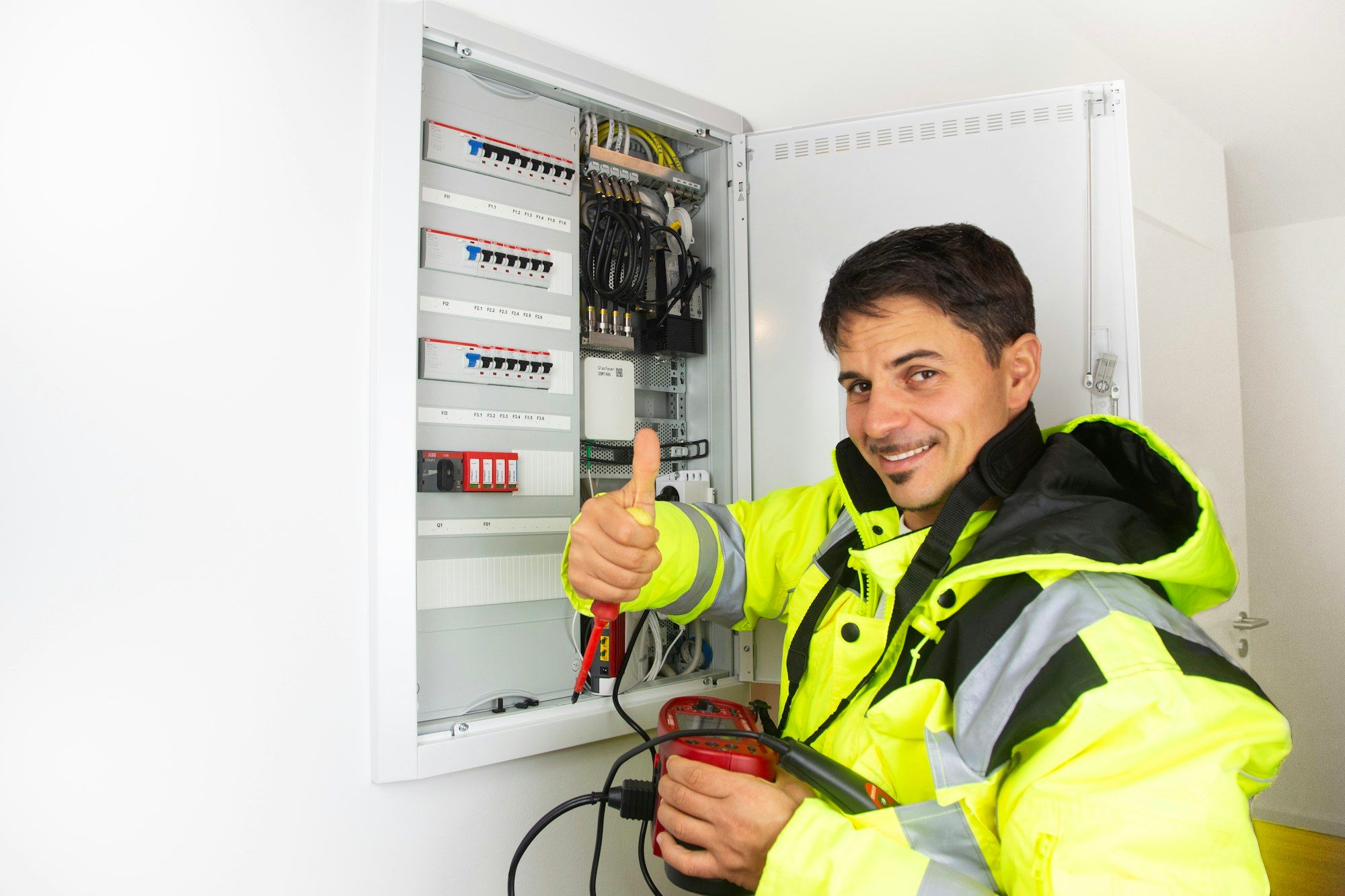 Electrician in a hi-vis jacket smiling next to an open switchboard